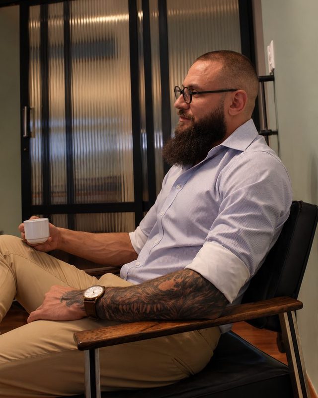Lucas Coutinho sentado numa poltrona do consultório, com uma xícara de café, sorrindo.